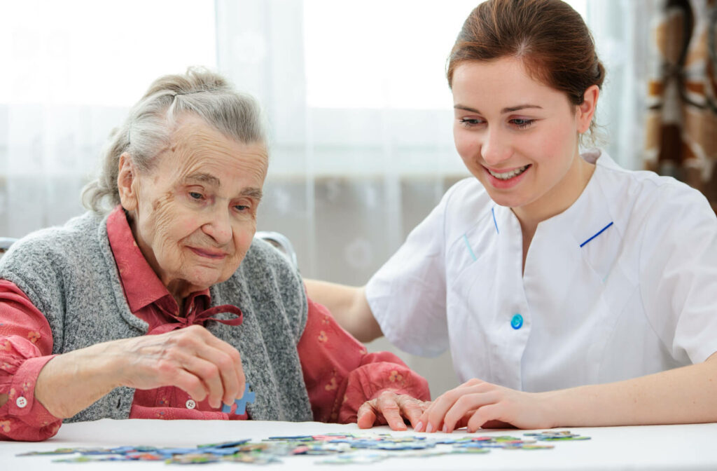 A  female caregiver patiently assists the senior woman in solving a jigsaw puzzle, fostering a delightful and engaging activity that brings joy and mental stimulation to their shared time.