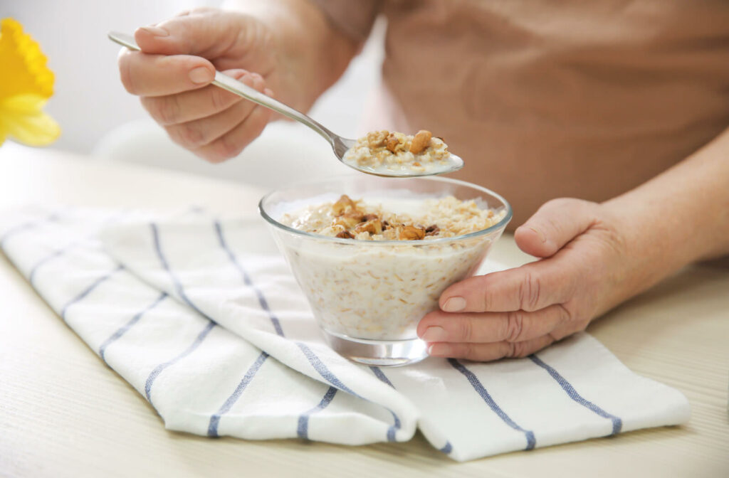 Close-up of a bowl of oatmeal with nuts resting on a tea towel as a person scoops up a spoonful to eat