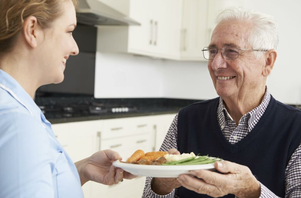 An older adult man smiling as he receives his lunch from an assisted living staff member.