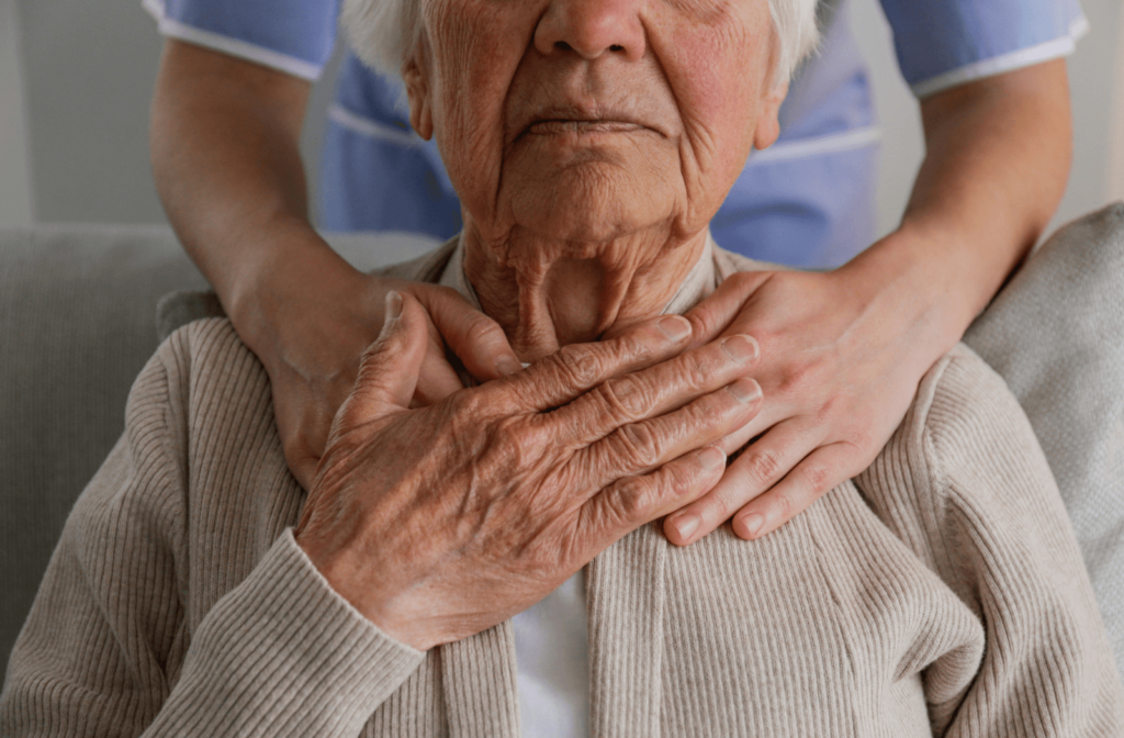 A senior sits in front of an adult, holding one hand to their collarbone.